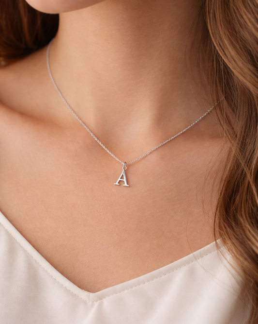 Silver necklace with a letter 'A' pendant on a person wearing a white top.