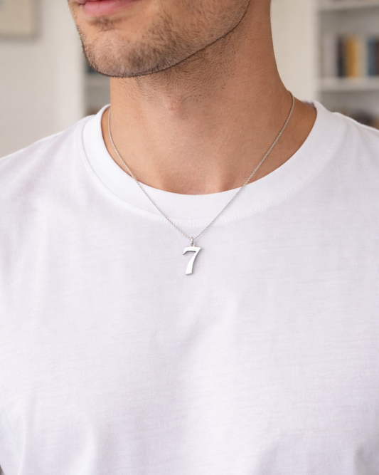 Man wearing a silver necklace with a '7' pendant on a white shirt.