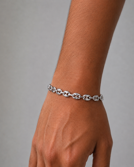 Silver chain bracelet on a wrist against a gray background