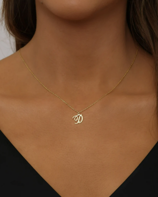 A woman wearing a black v-neck shirt showcasing a silver initial charm letter necklace.