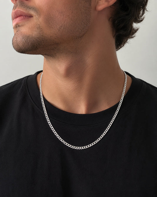 Man wearing a silver chain necklace against a neutral background