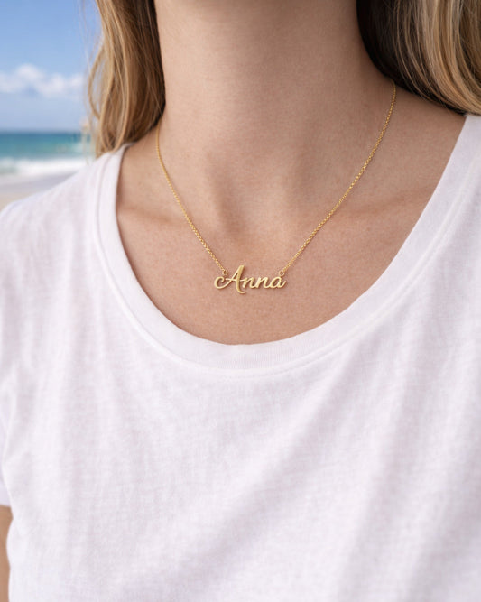 Person wearing a gold necklace with 'Anna' on a beach
