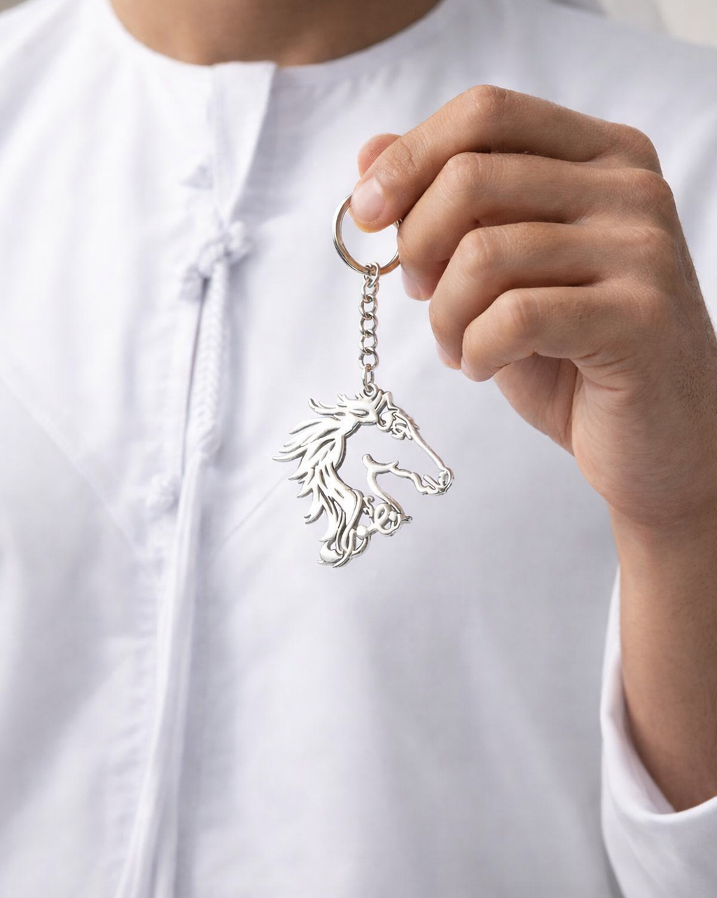 Person holding a silver keychain with a horse design against a neutral background