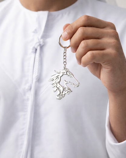 Person holding a silver keychain with a horse design against a neutral background