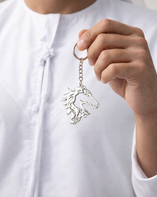 Person holding a silver keychain with a horse design against a neutral background