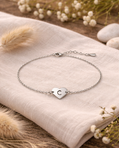 Silver bracelet with a heart-shaped charm on a beige fabric background