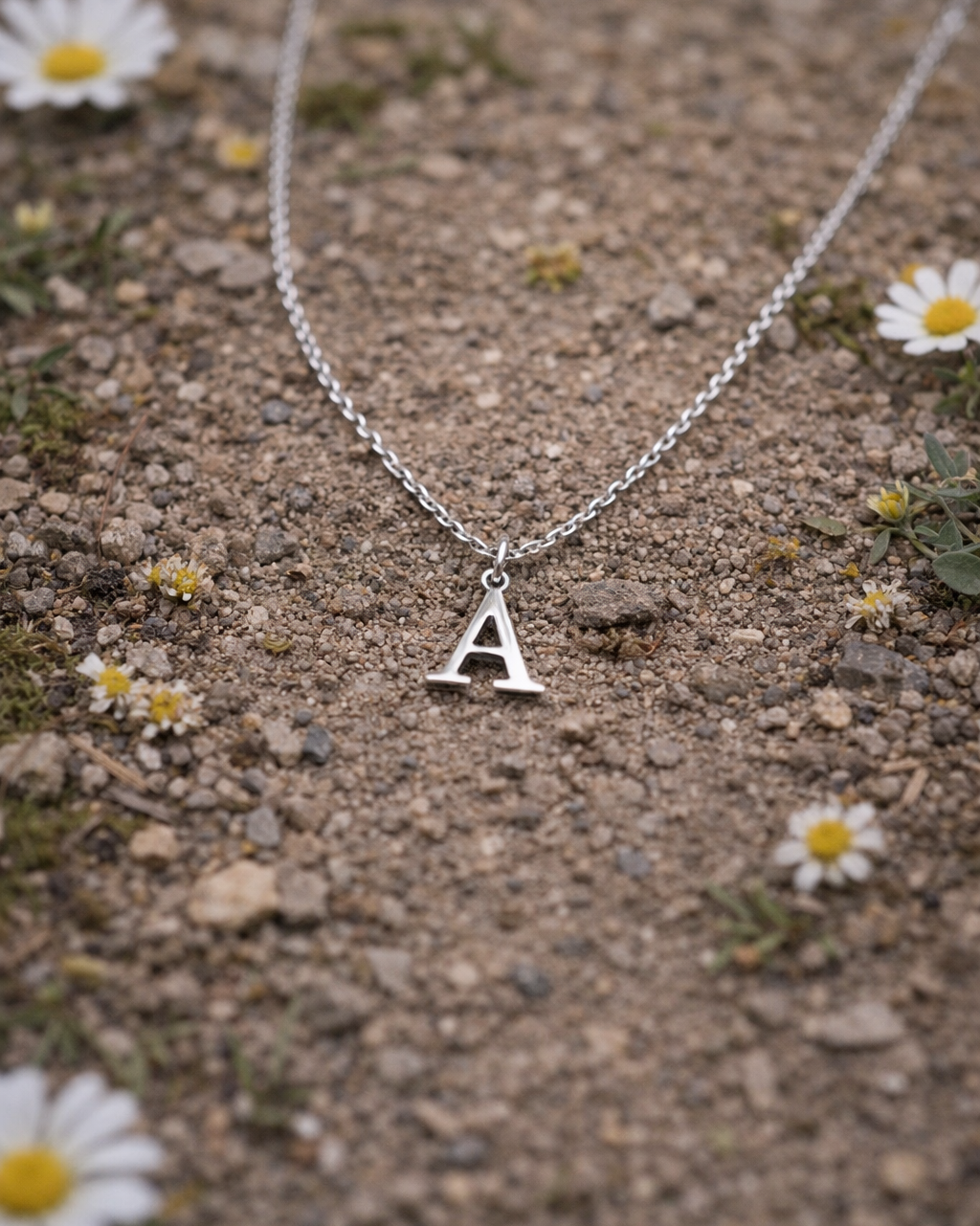 Silver necklace with a 'A' pendant on a ground surface with small flowers.