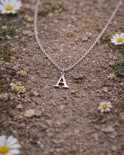 Silver necklace with a 'A' pendant on a ground surface with small flowers.