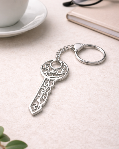 Silver key-shaped keychain on a light surface with a cup and glasses in the background