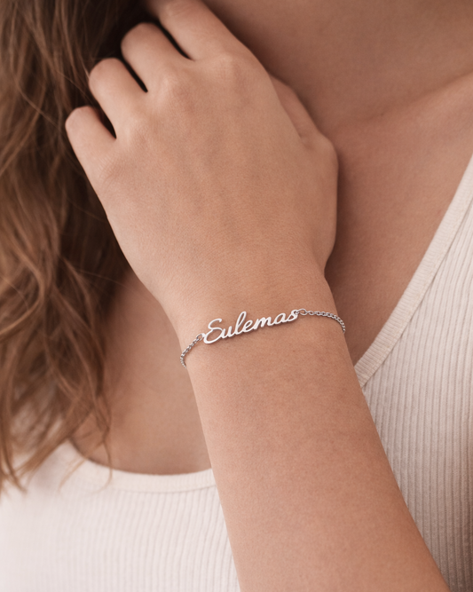 Silver bracelet with 'Eulemas' on a person's wrist, wearing a white tank top.