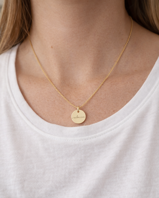 Person wearing a gold necklace with a round pendant on a white shirt.