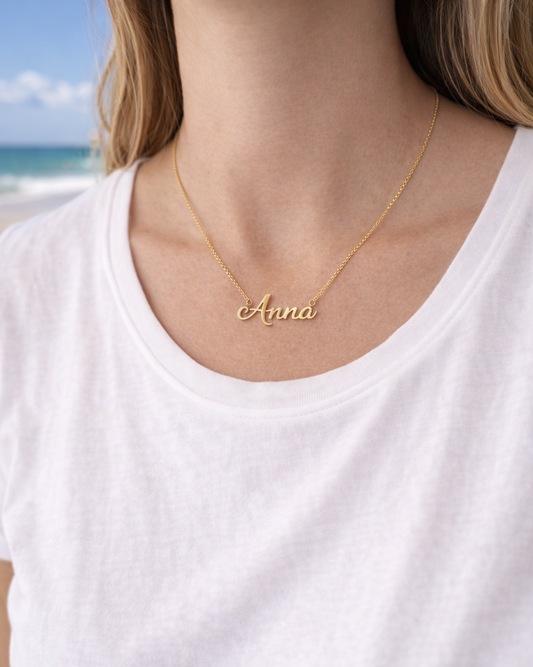 Person wearing a gold necklace with 'Anna' on a beach