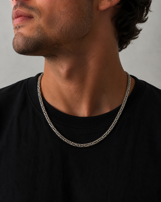Man wearing a silver chain necklace against a neutral background