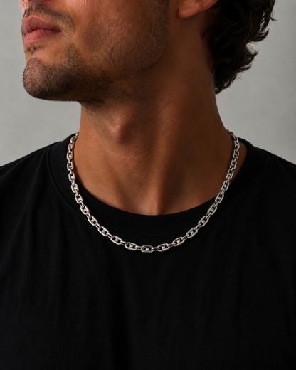 Man wearing a silver chain necklace against a neutral background