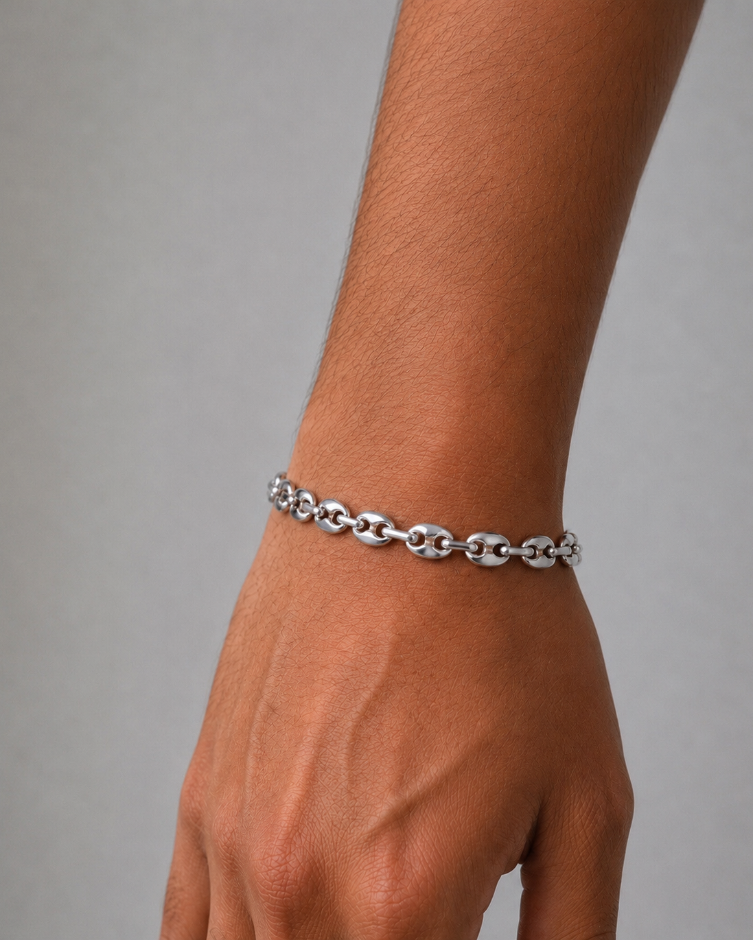 Silver chain bracelet on a wrist against a gray background