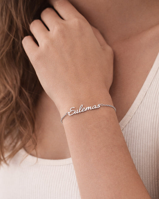 Silver bracelet with 'Eulemas' on a person's wrist, wearing a white tank top.