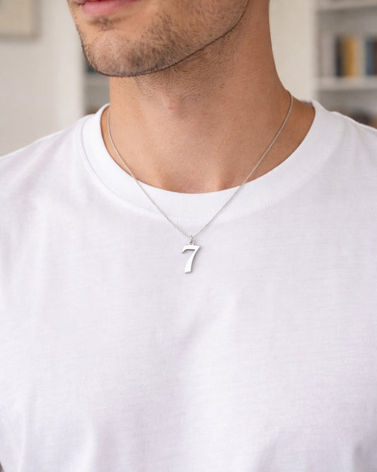 Man wearing a silver necklace with a '7' pendant on a white shirt.