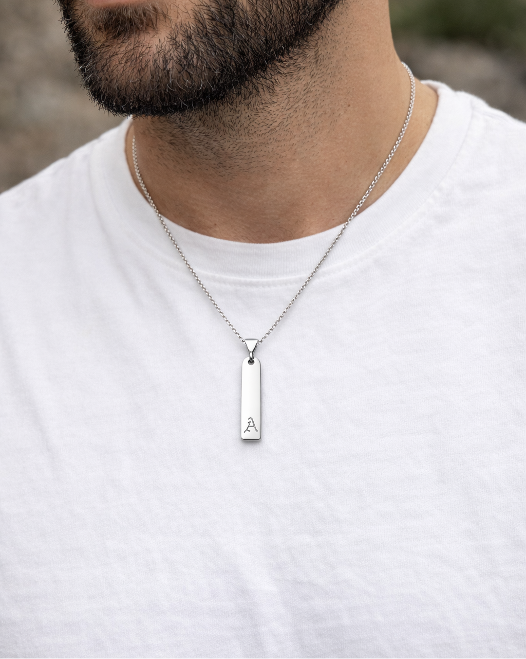 Man wearing a silver necklace with a pendant on a blurred natural background
