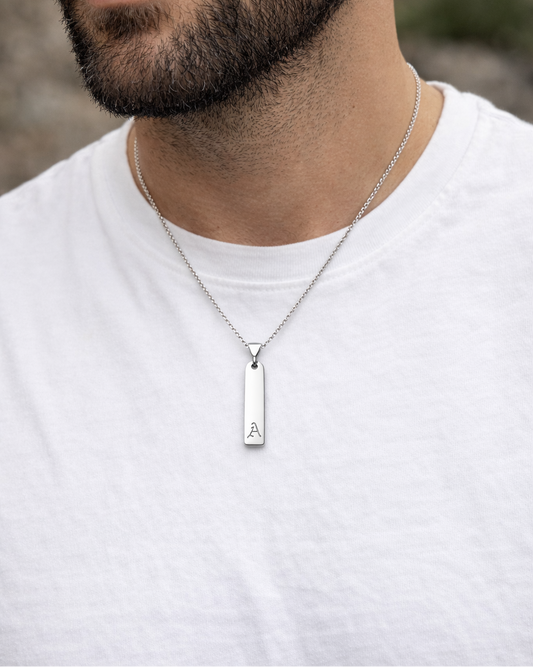Man wearing a silver necklace with a pendant on a blurred natural background